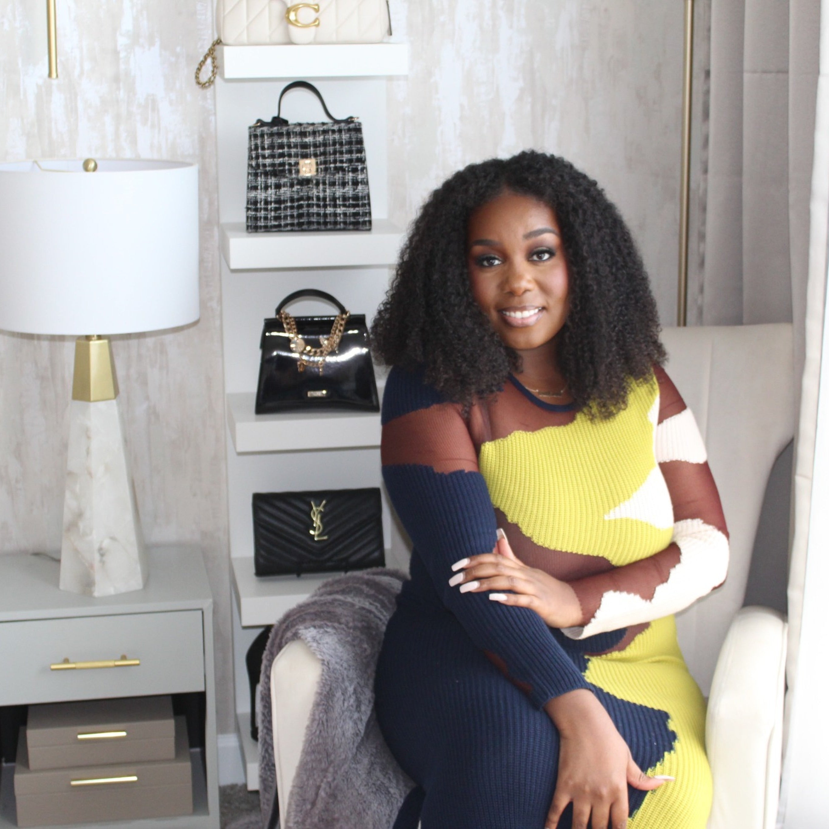 Woman sitting on a couch in a stylish room with bags displayed on shelves.