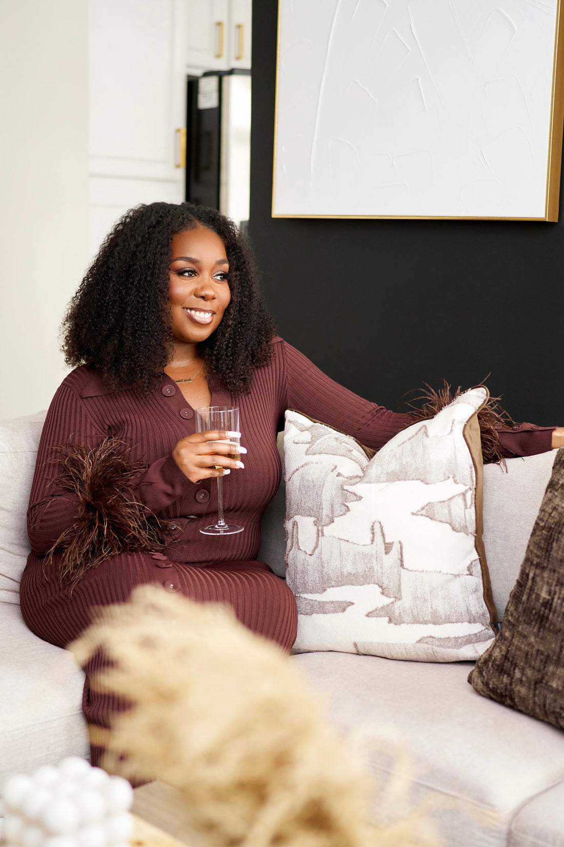 Woman sitting on a couch holding a glass of wine, surrounded by decorative pillows.