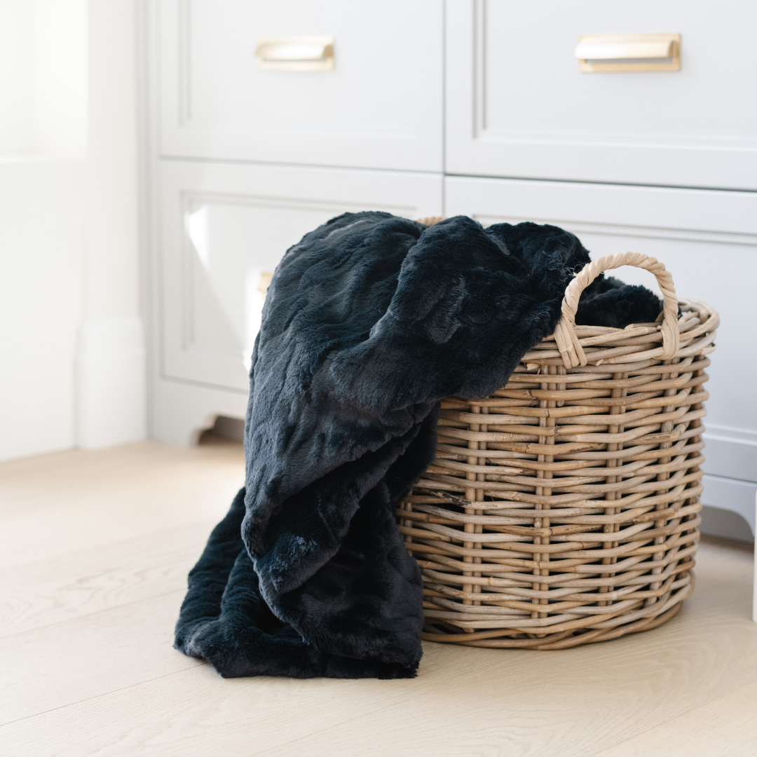 Black blanket draped over a wicker basket in a room with white cabinets.