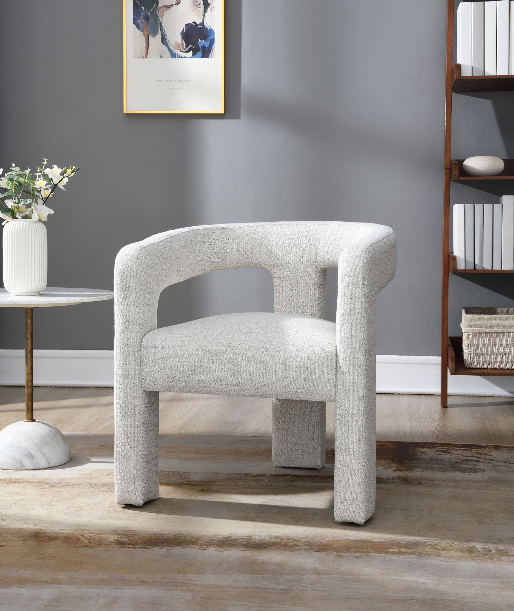 Gray armchair in a room with a gray wall, small table, and bookshelf.