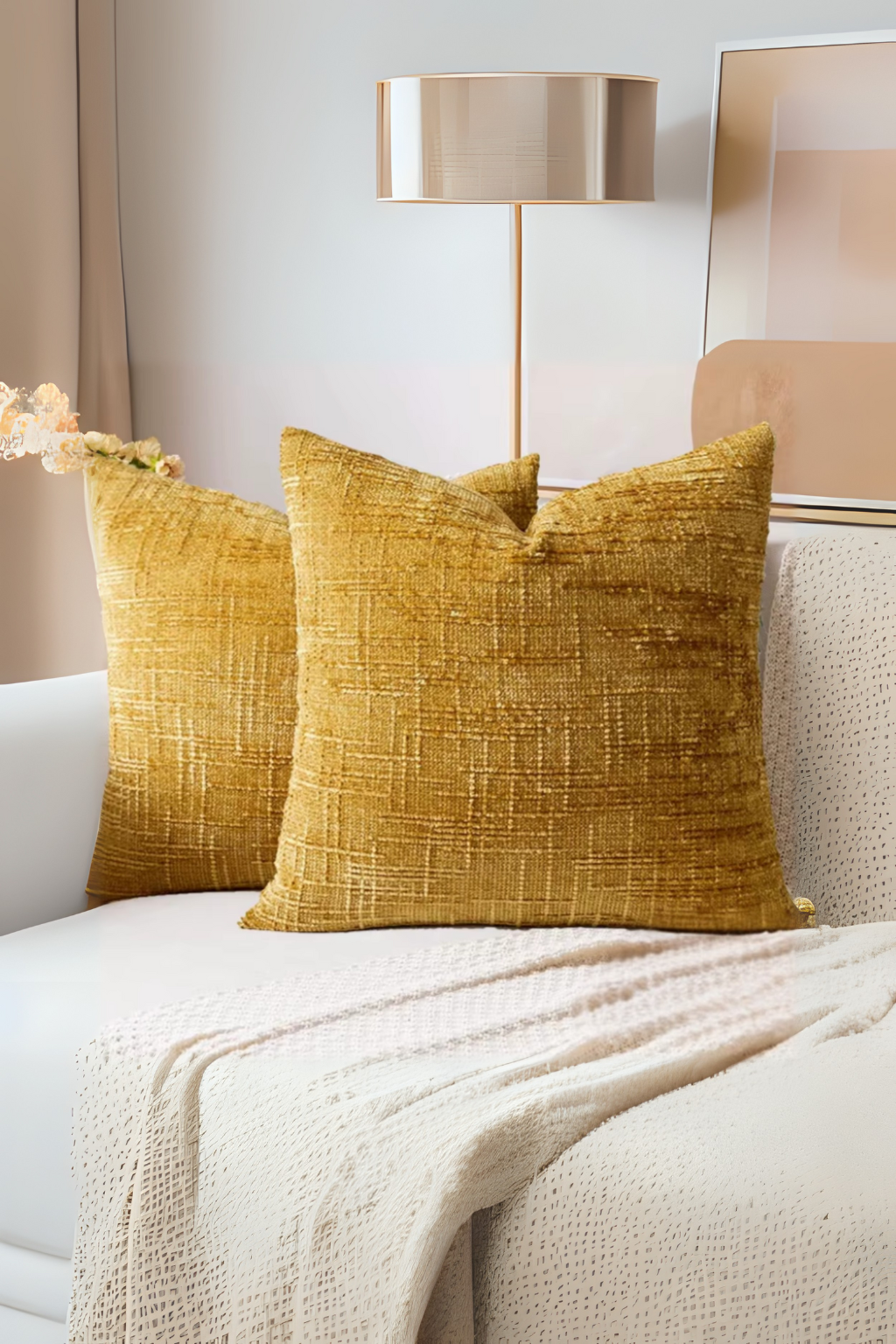 Two mustard yellow textured pillows on a white sofa with a lamp and abstract painting in the background.