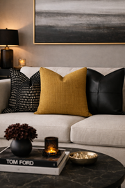 Decorative living room with a beige sofa, black, yellow, and white pillows, and a coffee table with a book and decorative items.