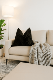Beige sofa with a black pillow and knitted blanket in a living room setting.