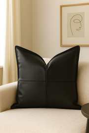 Black leather pillow on a beige sofa with a neutral wall and abstract art in the background