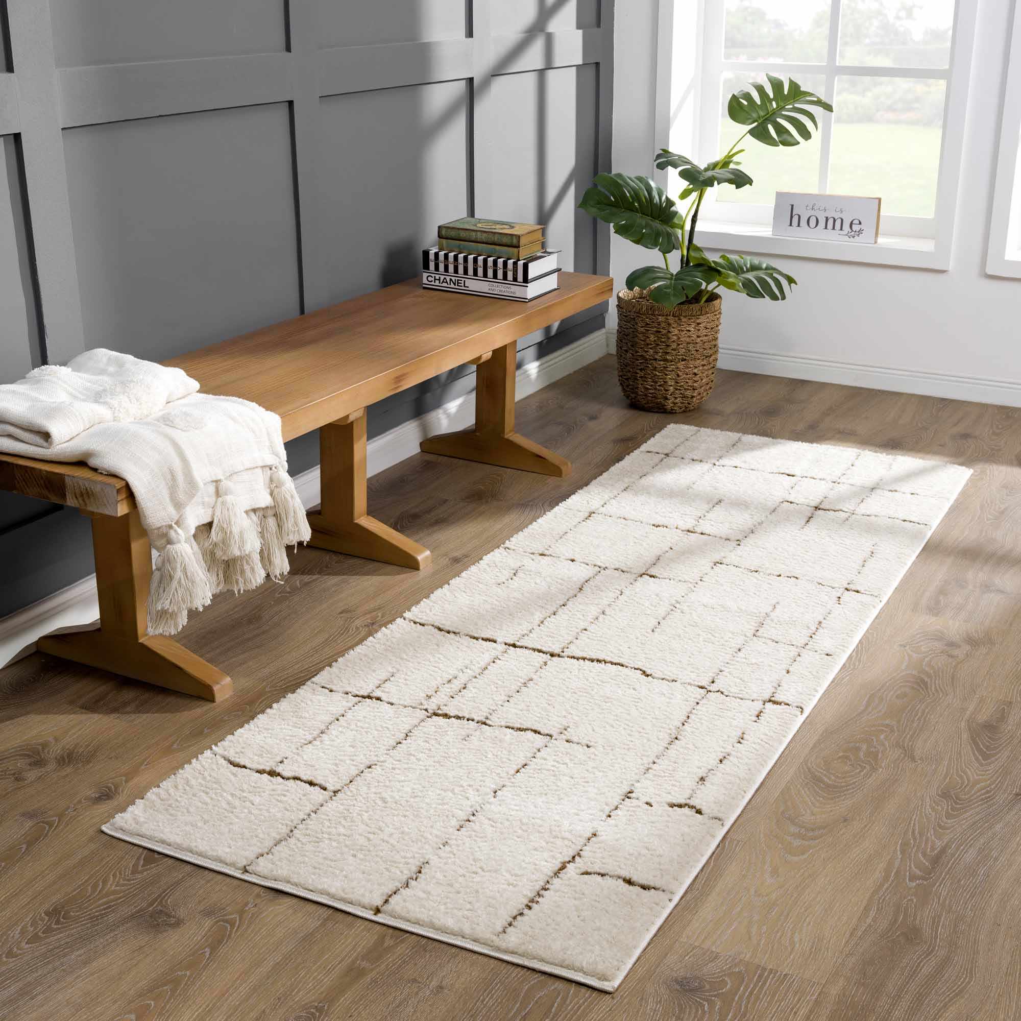 Beige runner rug on a wooden floor with a bench and plant in the background.