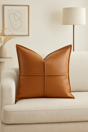 Brown leather pillow on a beige sofa with a lamp and abstract art in the background.
